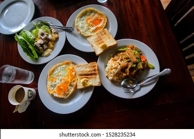 Breakfast Set For Two Including Fresh Green Salad,sunny Side Up Eggs,bread,Thai Fried Rice,Thai Stir Fried Noodles And Coffee.Top View.