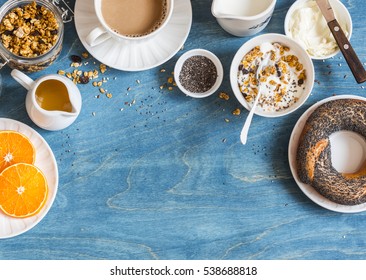 Breakfast setting over blue table with copy space border. Yogurt, pumpkin granola, bagel, butter. Top view. Flat lay