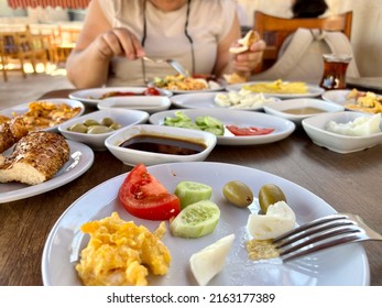 Breakfast, Side View Traditional Turkish Breakfast Spread On Table In Turkey. Turkish Food For Brunch On Plate With Selective Focus Over Blurred Woman Eating On Table Local Food In Turkey