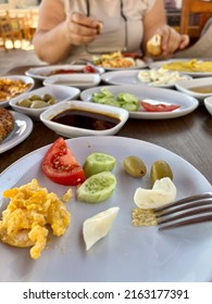 Breakfast, Side View Traditional Turkish Breakfast Spread On Table In Turkey. Turkish Food For Brunch On Plate With Selective Focus Over Blurred Woman Eating On Table Local Food In Turkey