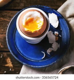 Breakfast with soft-boiled egg, served with bread over old wooden table. Top view. Square image with selective focus