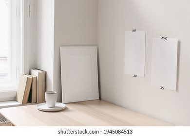 Breakfast Still Life. Cup Of Coffee, Books On Wooden Desk, Table Near Window. Empty Notepads, Posters Taped On White Wall.Blank Picture Frame Mock-up. Elegant Scandinavian Working Space, Home Office.