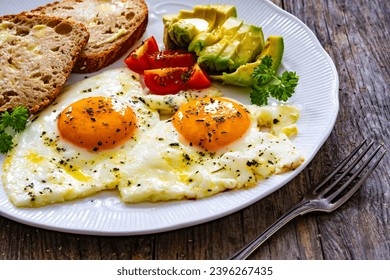 Breakfast - sunny side up egg, toasted bread and avocado served on wooden table  - Shutterstock ID 2396267435