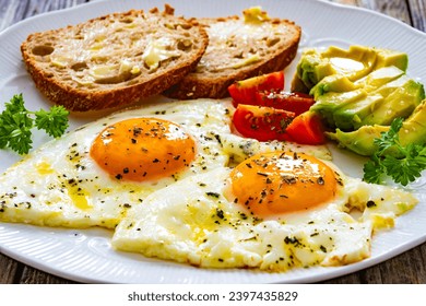 Breakfast - sunny side up egg, toasted bread and avocado served on wooden table  - Powered by Shutterstock