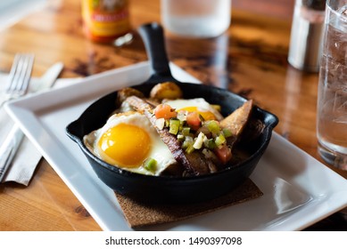 Breakfast Sunny Side Up and Potatoes in a Black Skillet on a White Plate for Brunch on a Brown Wooden Table Top