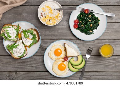 Breakfast table with healthy food. Fried eggs, salad of spinach leaves, avocado, oatmeal, cheese sandwich, poached eggs and orange juice, top view