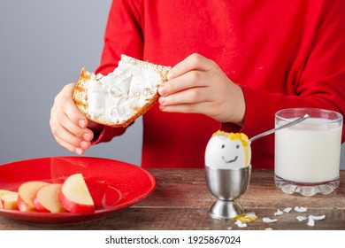 Breakfast table with simple balanced nutritious ingredients. A soft boiled egg with face painted on, a slice of toasted bread with cream cheese spread, apple, a glass of milk with a girl eating. - Powered by Shutterstock