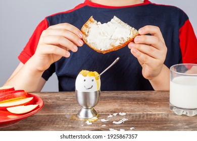 Breakfast Table With Simple Balanced Nutritious Ingredients. A Soft Boiled Egg With Face Painted On, A Slice Of Toasted Bread With Cream Cheese Spread, Apple, A Glass Of Milk And A Boy Eating There