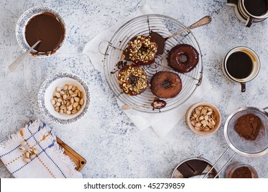 Breakfast table with sweets and coffee. Four tasty freshly baked donuts glazed with chocolate on cooling rack with nuts bowl  and chocolate cream bowl of rustic old marble table.  - Powered by Shutterstock