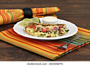 Breakfast Taco With Scrambled Eggs, Shredded Cheese, Chorizo, Peppers And Onions With A Side Of Lime Slices And Sour Cream.  Selective Focus On Front Of Taco.