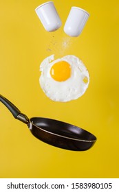 Breakfast Time. A Fried Egg And A Frying Pan With Salt Shakers Levitate In The Air On A Yellow Background