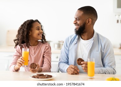 Breakfast Time. Portrait of cheerful African American little girl and man eating cookies and looking at each other, dad and daughter sitting at dinner table in kitchen, enjoying meal with orange juice - Powered by Shutterstock