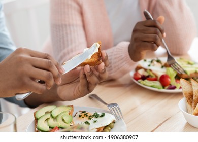 Breakfast Time. Unrecognizable African American Couple Enjoying Tasty Food In Kitchen, Sitting At Table, Having Delicious Meal In The Morning, Man Spreading Butter On Bread, Cropped Image, Closeup - Powered by Shutterstock