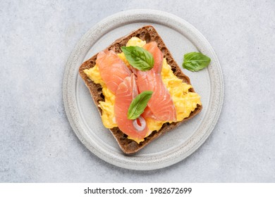 Breakfast Toast With Scrambled Eggs And Smoked Salmon Lox On Grey Plate, Top View. Isolated On Grey Concrete Background. Tasty Healthy Sandwich With Egg And Salmon