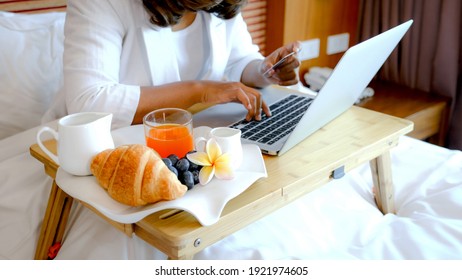 Breakfast in a tray on the bed in the luxury hotel room in front of an Asian businesswoman traveler work with laptop, healthy food concept.