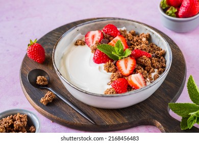 Breakfast, unsweetened yogurt with chocolate baked granola and chopped fresh strawberries in a gray bowl on a pink concrete background. Breakfast recipes. Healthy food - Powered by Shutterstock