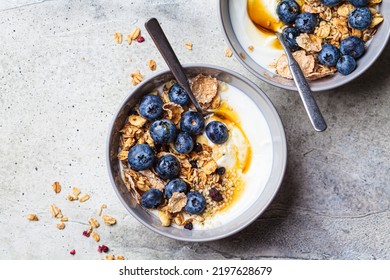 Breakfast yogurt bowl with granola, blueberries and maple syrup, gray background, top view, copy space. Healthy food concept.