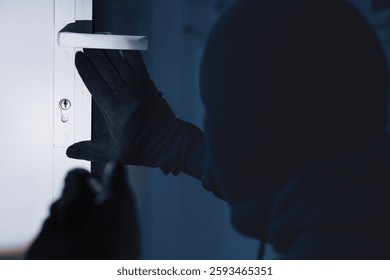 Break-In Concept. Back view of unrecognizable criminal in black balaclava entering victim's house, using torch on lock