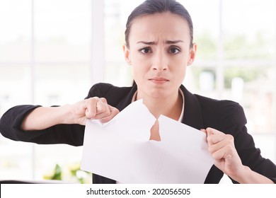 Breaking contract. Furious young woman in formalwear tearing up paper while sitting at the table