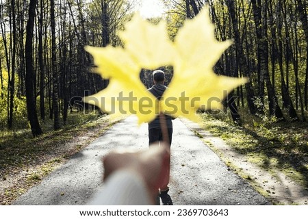 Breaking up couple. concept. Man going away in autumn park through a hole in the form of heart of maple autumn leaf in a woman hand. 