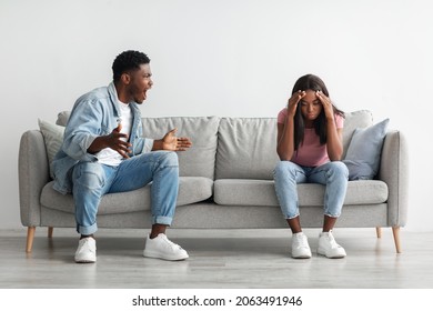 Breaking Up And Divorce Concept. Young married black couple having fight, guy yelling at crying lady, gesturing at home. Furious man shouting at his wife or girlfriend, sitting on sofa at living room