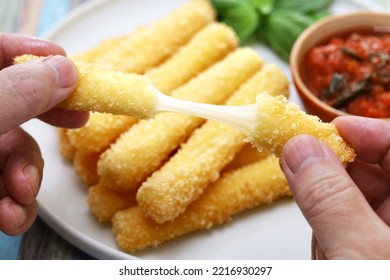 Breaking freshly fried mozzarella sticks and stretching cheese with both hands. - Shutterstock ID 2216930297