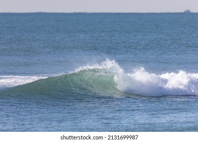 A Breaking Wave Seen In Profile, In The Shape Of A Tube Leaving A Wake Of Water In The Wind On A Sunny Day In The Mediterranean Sea, With A Boat On The Horizon. Horizontal. Ocean Conc