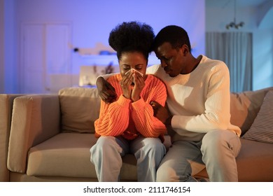 Breakup And Cheating. Young Black Couple Sitting On Sofa After Quarreling At Home, Loving African Man Husband Asking Forgiveness From Crying And Offended Wife. Family Relationship Difficulties