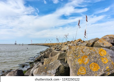 Breakwater Or Pier And Poles With Colored Rope And Plastic Waving In The Wind And A Ship In The Wadden Sea At The Entrance To The Port Of Harlingen The Netherlands                       