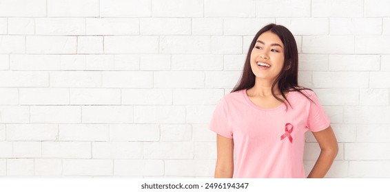 Breast Cancer. Asian Girl In Pink T-Shirt With Cancer Awareness Ribbon Posing Standing Over White Brick Wall Background. Empty Space - Powered by Shutterstock