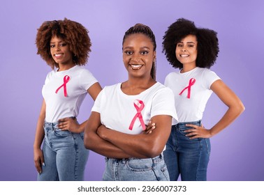 Breast Cancer Awareness Advertisement. Group Of Three African American Ladies With Pink Ribbons Over Purple Background, Studio Shot, Selective Focus. Oncology Nursing Month Concept - Powered by Shutterstock