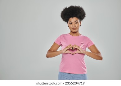 breast cancer awareness, african american woman with pink ribbon on grey backdrop, heart sign, smile - Powered by Shutterstock