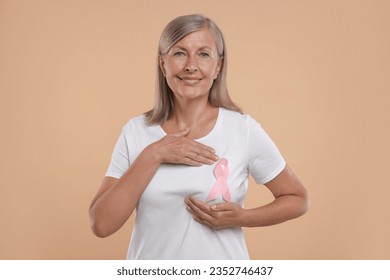 Breast cancer awareness. Beautiful senior woman with pink ribbon doing self-examination on light brown background - Powered by Shutterstock