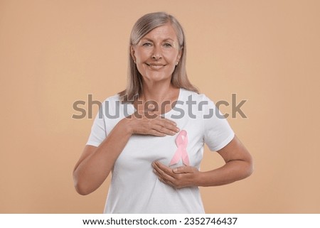 Breast cancer awareness. Beautiful senior woman with pink ribbon doing self-examination on light brown background