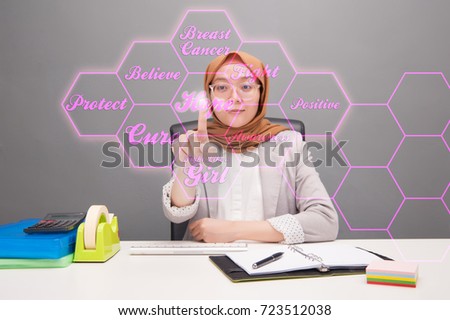 Breast cancer awareness concept.Selective focus of an asian young business woman wearing hijab pointing her finger to the graphic icon and related.Blurred background and artificial grain effect.