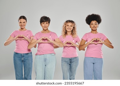 breast cancer awareness, happy interracial women with pink ribbons showing heart on grey, diversity - Powered by Shutterstock