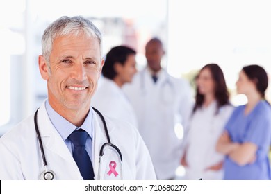 Breast cancer awareness ribbon against mature doctor standing upright while waiting for his team - Powered by Shutterstock