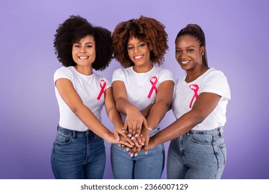 Breast Cancer Awareness. Three Smiling Black Ladies With Pink Ribbons Joining Hands In Stack Over Purple Studio Background. Fighting Oncology Together Concept, Support Group