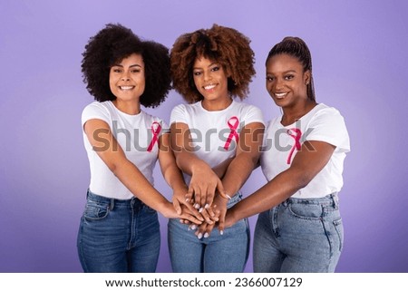 Breast Cancer Awareness. Three Smiling Black Ladies With Pink Ribbons Joining Hands In Stack Over Purple Studio Background. Fighting Oncology Together Concept, Support Group