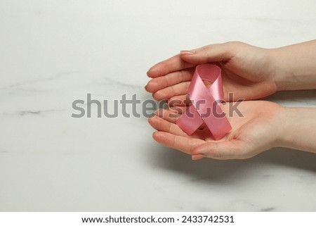 Breast cancer awareness. Woman with pink ribbon at white marble table, top view. Space for text