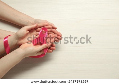 Breast cancer awareness. Women holding pink ribbon at white wooden table, top view. Space for text