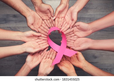 Breast cancer concept. Group of people in hands holding pink paper ribbon on brown wooden background - Shutterstock ID 1831455025