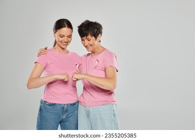 breast cancer concept, happy women with pink ribbons fist bumping on grey backdrop, cancer free - Powered by Shutterstock