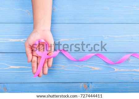 Breast Cancer concept : Woman holding Pink ribbon symbol of breast cancer on blue wooden table background. Free space for text or design. Top view