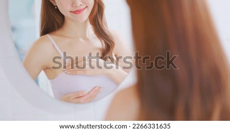 breast cancer self check concept -  asian woman is touching her chest to prevent sick while looking in mirror at home
