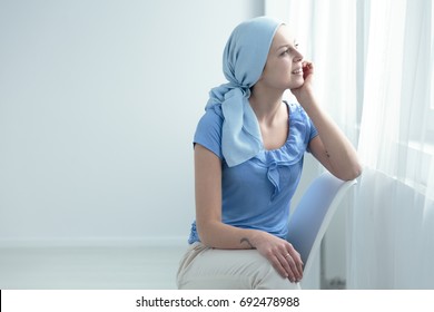 Breast cancer survivor sitting on a white chair, happily looking out the window - Shutterstock ID 692478988