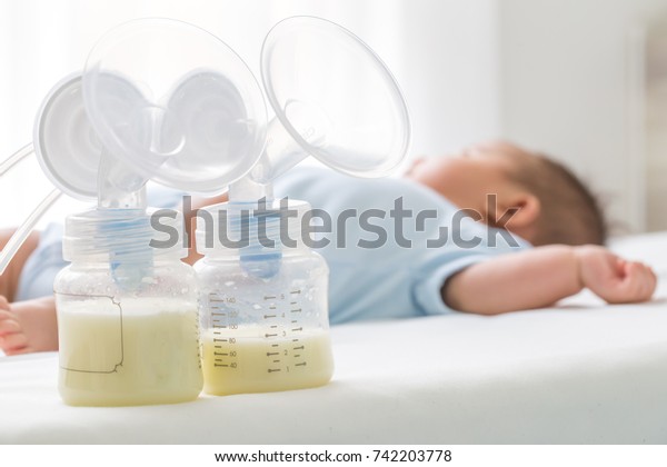 Breast milk\
pump and baby lying on the white\
bed