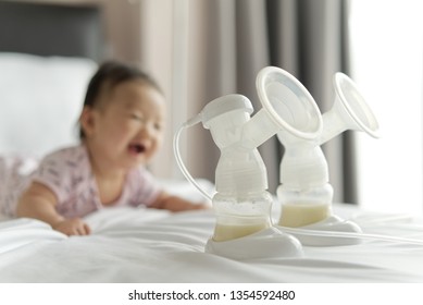 Breast milk in milk pump's bottles on the bed with smiling baby crawling in background. The milk got from milk pump's machine and ready for the baby. Baby health care concept.