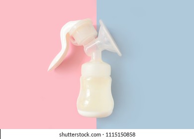 Breast pump bottle of milk for newborn baby over pink and blue pastel colors background. Maternity and baby care concept. Girl or boy. Top view.