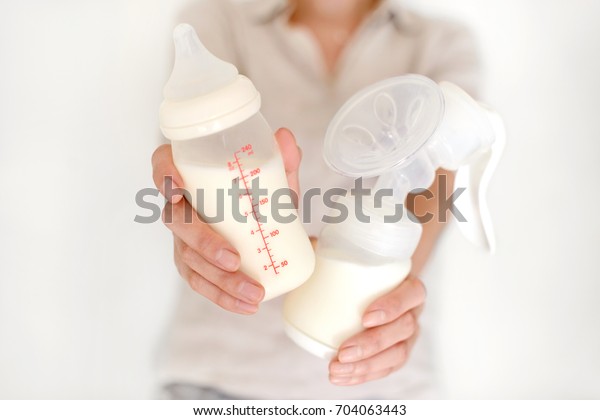 Breast pump and bottle with milk in woman\'s\
hand in blurred\
background